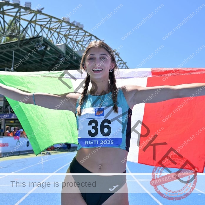 Margherita Castellani, a smiling female sprinter, holds up an Italian flag behind her on a blue track, wearing teal and bib number 36.