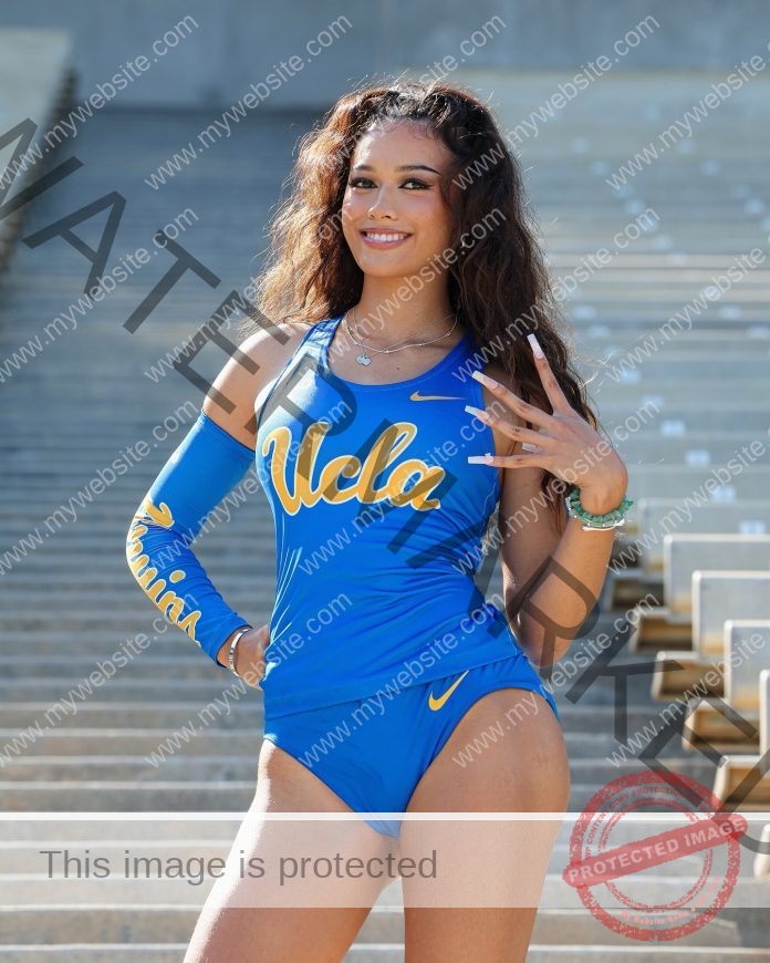 Sophia Hartwell, in a blue UCLA track outfit, smiles confidently on stadium steps, holding up four fingers with wavy hair and Bruins sleeve.