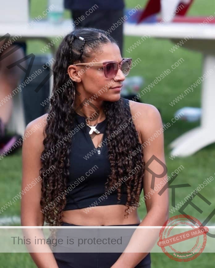 Saliyya Guisse standing near the track in her sunglasses, and a black upscale outfit.
