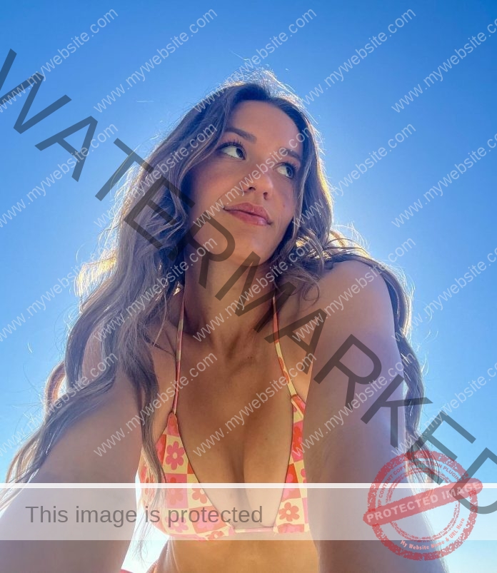 Sarah Lindenthal taking a selfie from blow, sun shining behind her, wearing a yellow and orange patterned bikini and a coy smile.