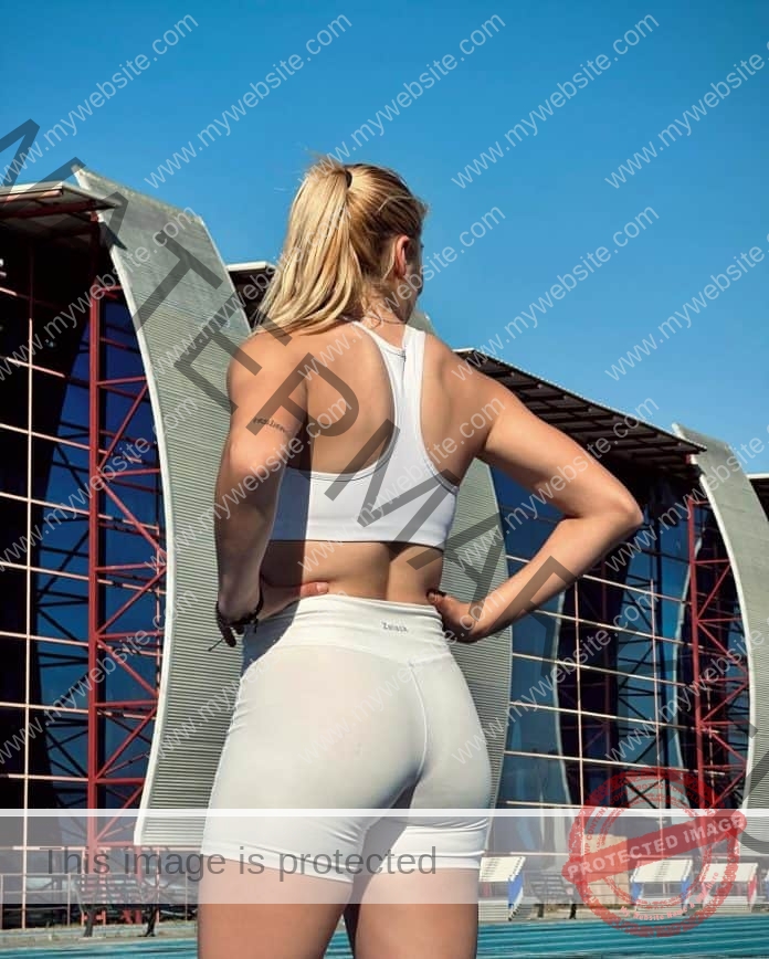 Andrea Martinez facing away from the camera, wearing a tight white sports bra and tight white shorts.