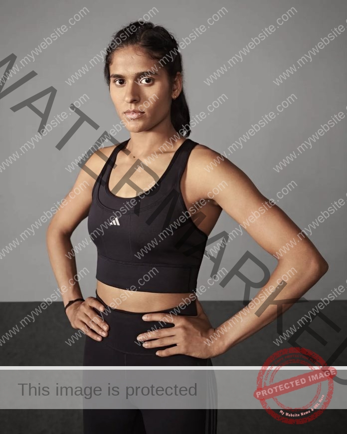 Shaili Singh stands with hands on her hips for a phot shoot, wearing all black and a white background.