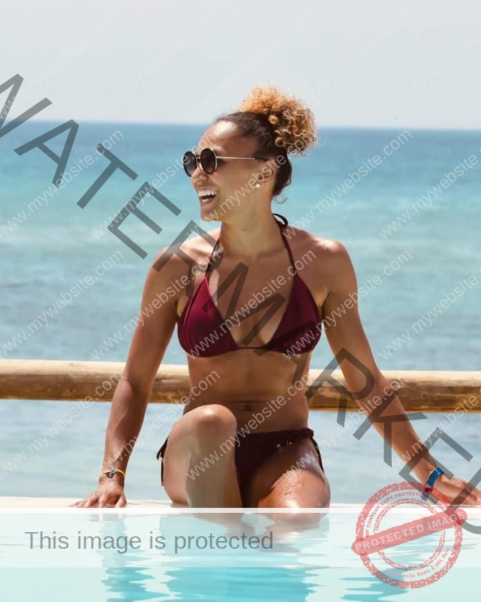 Angelica Berriot relaxing in a pool next to the ocean in a maroon two-piece bikini