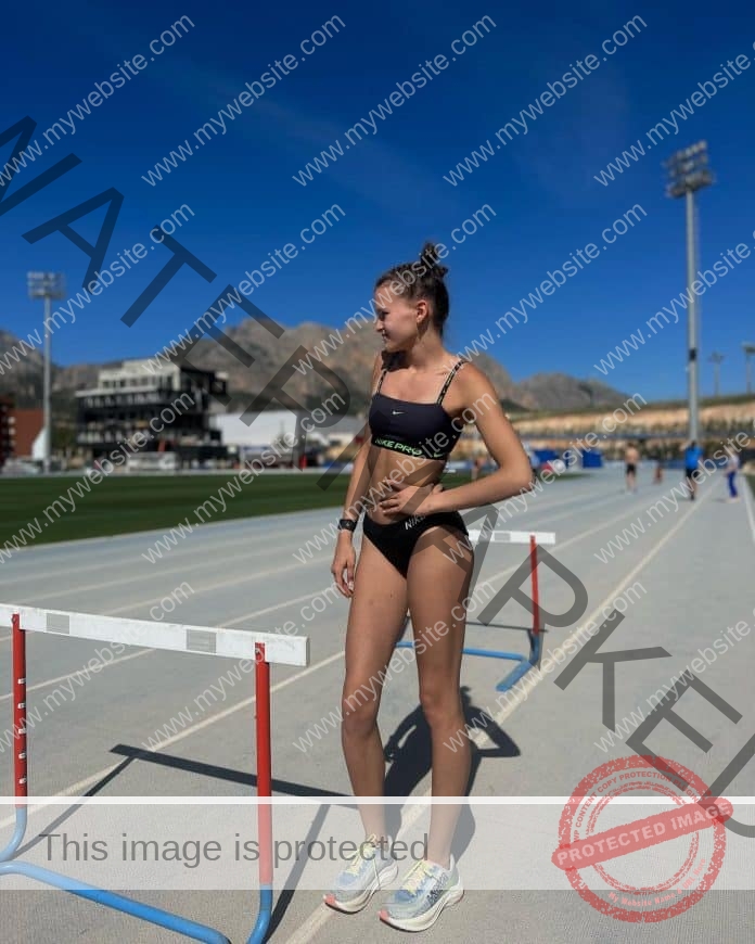 Anhela Luse standing between hurdles on the track, wearing a tight black track suit.