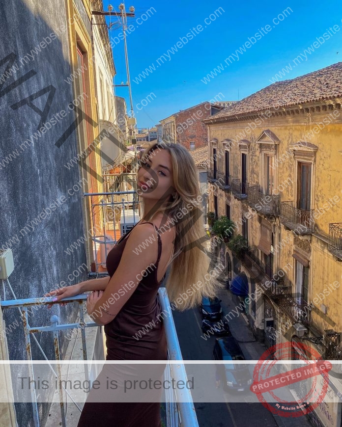 Olga Pietrzak standing on the balcony,leaning against a railing in a black dress and smiling.