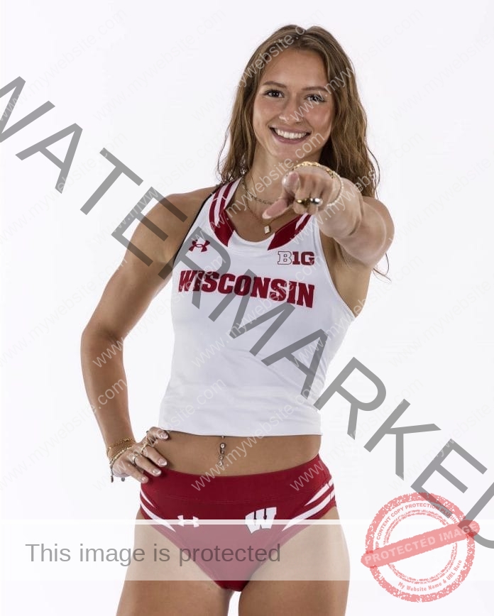 Shaina Zinter in front of a white background, wearing her college track uniform and pointing at the camera with a big smile.