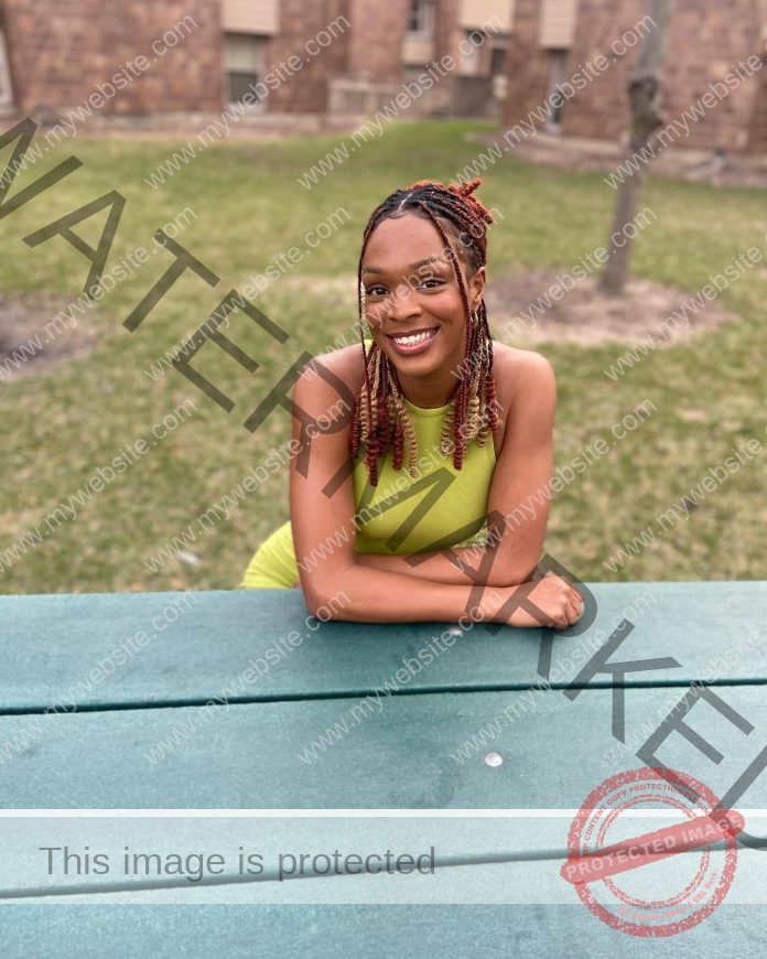 Shaniah Johnson wearing a yellow dress and leaning her forearms on a picnic table outdoors.