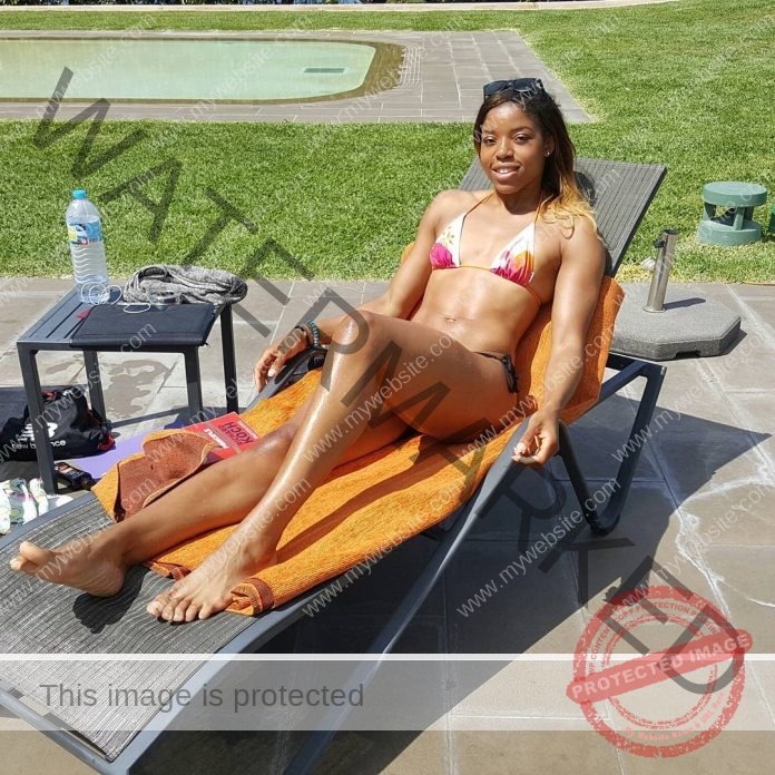 Abigail Irozuru lounging in a lounge chair in the sun, wearing a string bikini and smiling.