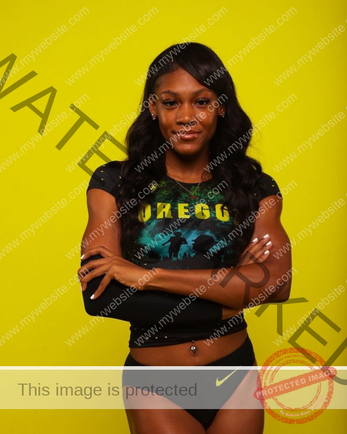 Aaliyah McCormick with a yellow background, standing arms folded for a photo shoot in her Oregon track uniform.