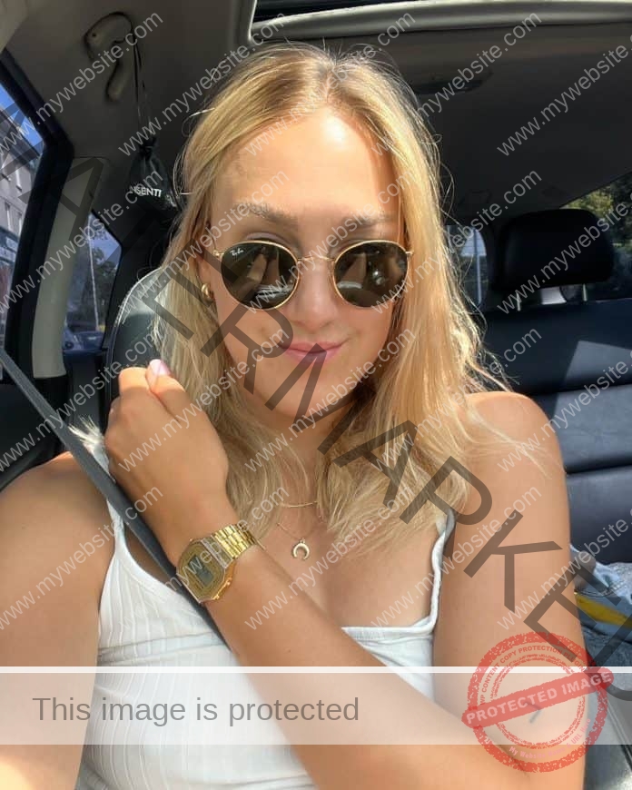 Paulina Ligarska posing for a selfie in a car, wearing sunglasses and a white tank top.