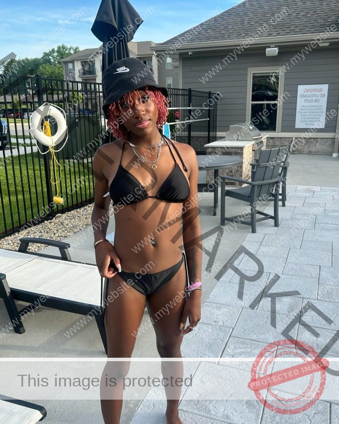 Kyndall Spain relaxes by the pool in a black bikini and a bucket hat