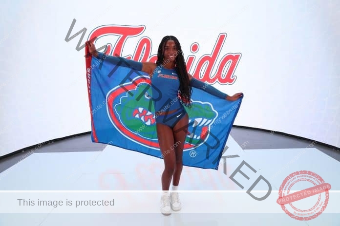 Gabrielle Pierre wearing her Florida Gators track outfit and holding a Florida Gators flag behind her, posing for a photo shoot.