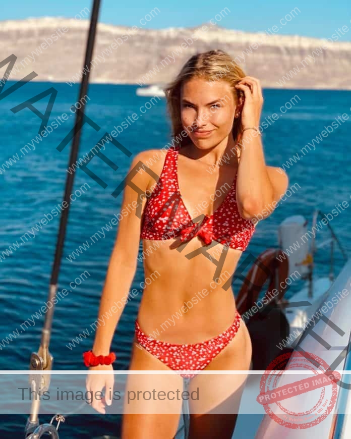 Pippi Lotta Enok standing on a boat, playing with her hair and wearing a red and white floral bikini.