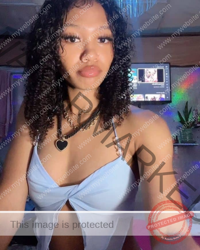 Princess Browne taking a selfie in a room, wearing a light blue crop top with a slit in the front.