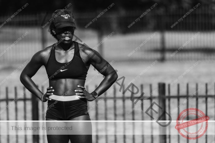 Raelyn Roberson posing in a black and white photo, hands on hips, in her track workout uniform at the track.