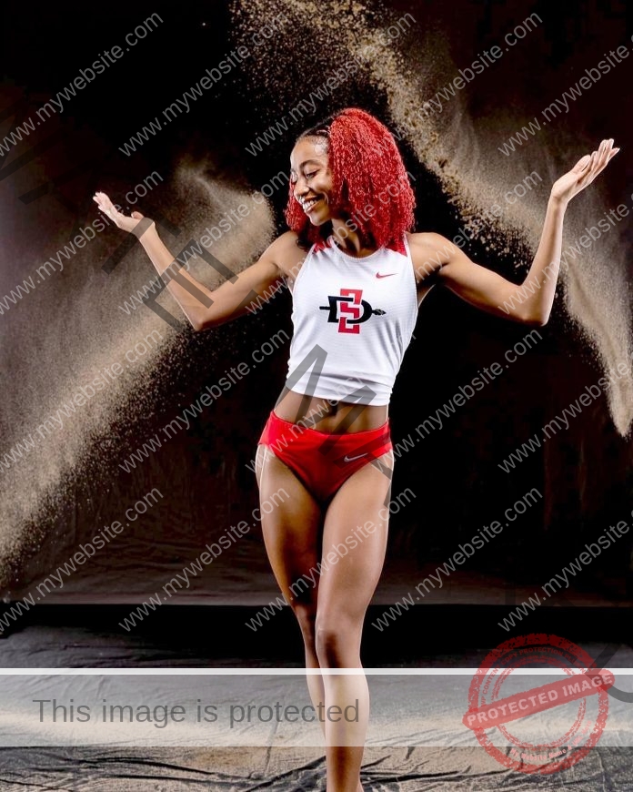 DeJanae Thompson posing for a photo shoot wearing her track uniform and arms raised.