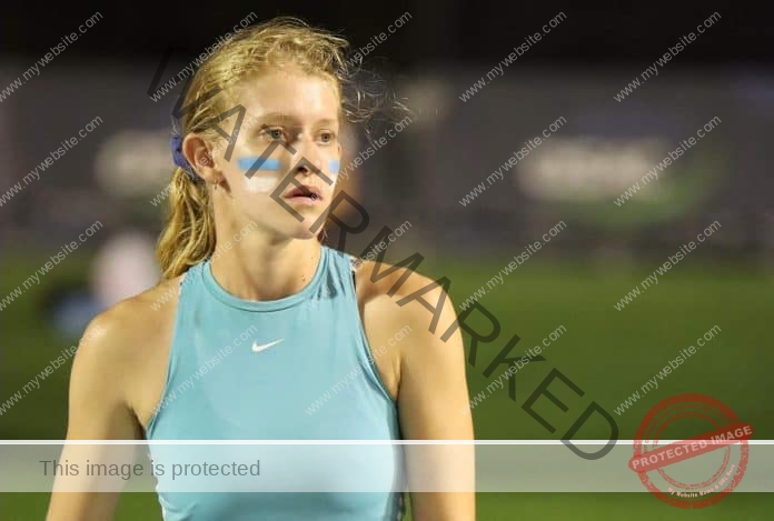 Amber Nyssen at a track meet wearing a blue sports bra, with stripes painted on her cheeks.