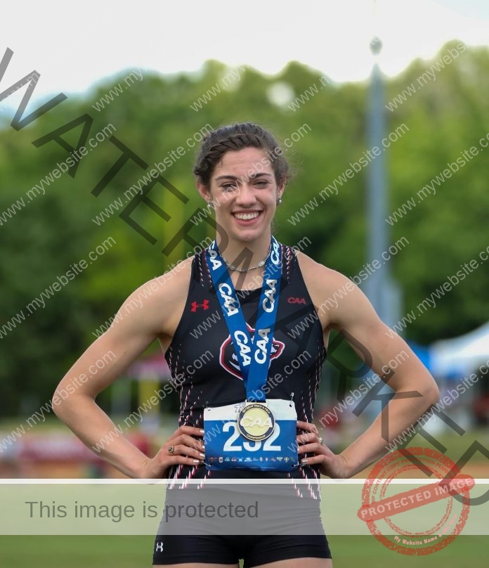 Dominique Biron standing with hands on hips by the track, wearing a medal.