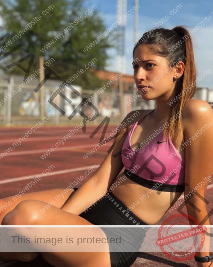 Lulu Arguello sitting on the track in her pink and black track kit, looking focused.