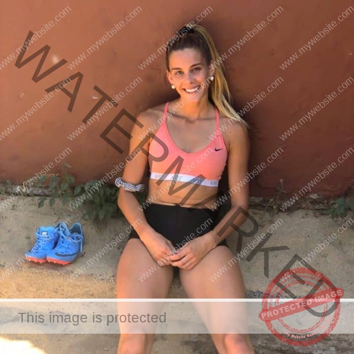 Isi Jiménez sitting against a wall after a workout, wearing a pink and white sports bra, black shorts and a smile.