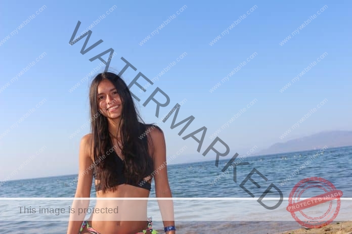 Belén Ituarte Araya of Chile standing on the beach in front of the ocean, wearing a black swimsuit and a smile.