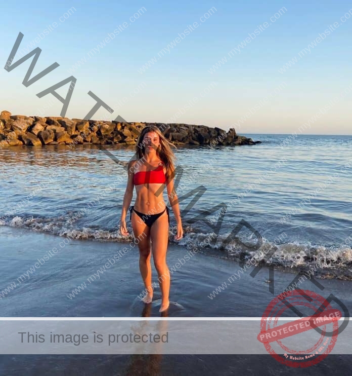 Aylen Zarategui of Argentina standing int eh surf, wearing a red bikini top and black bottoms.