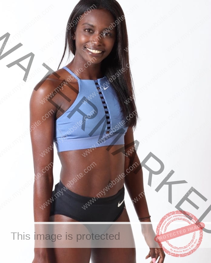 Evelise Veiga posing for a photo with a white background, wearing a blue sports bra and black shorts - smiling big.