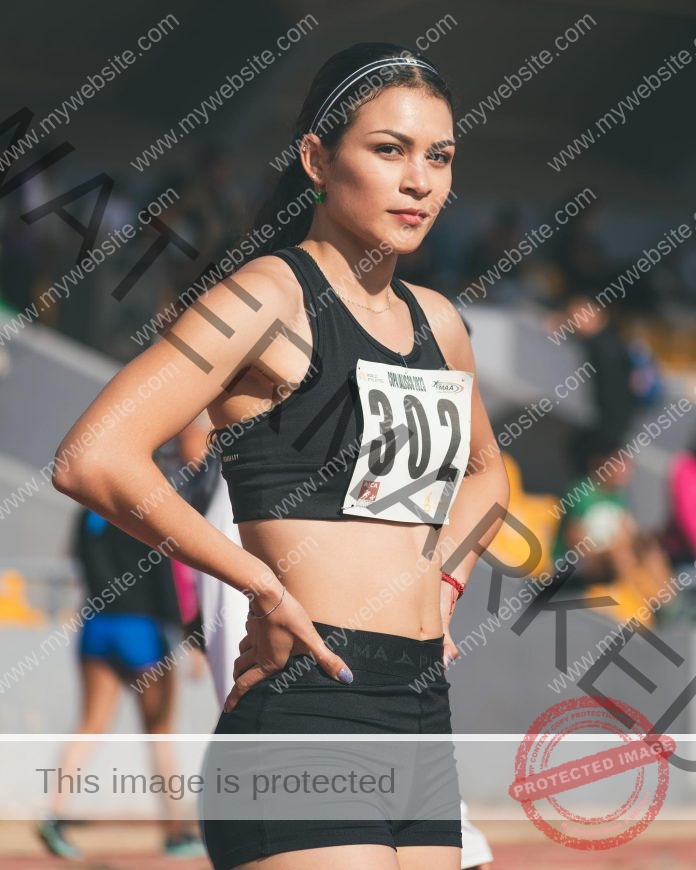 Yareli Valdivia wearing her track uniform and number 302, stands with hands on hips ready to run.