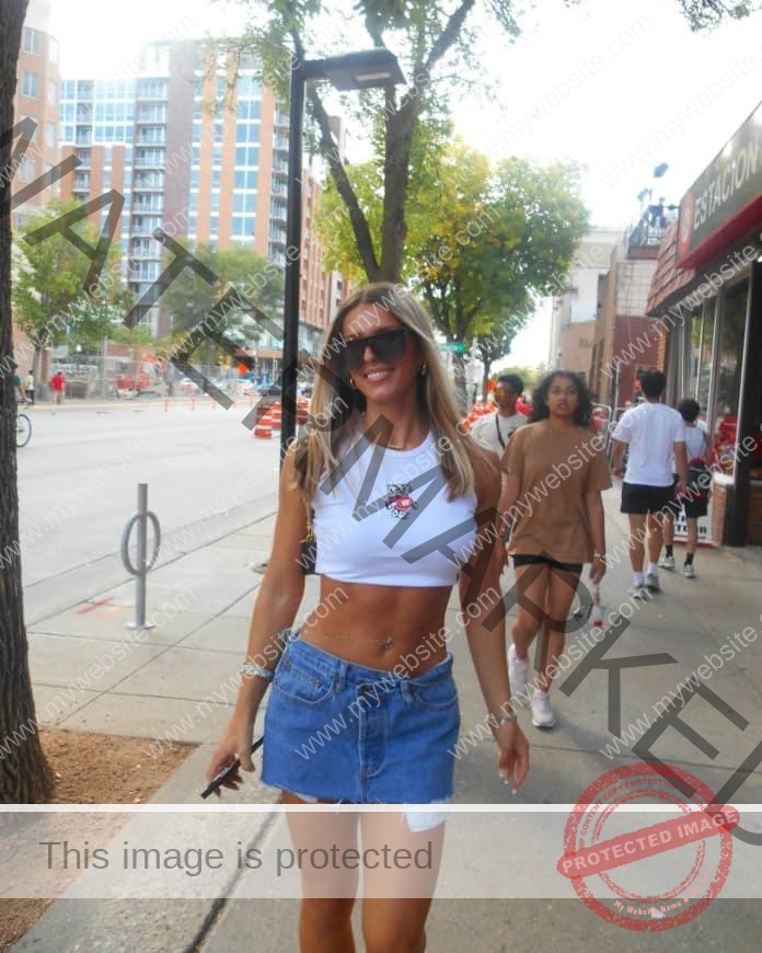 Mila Puseljic posing on a sidewalk, wearing a white crop top, jean skirt and sunglasses.