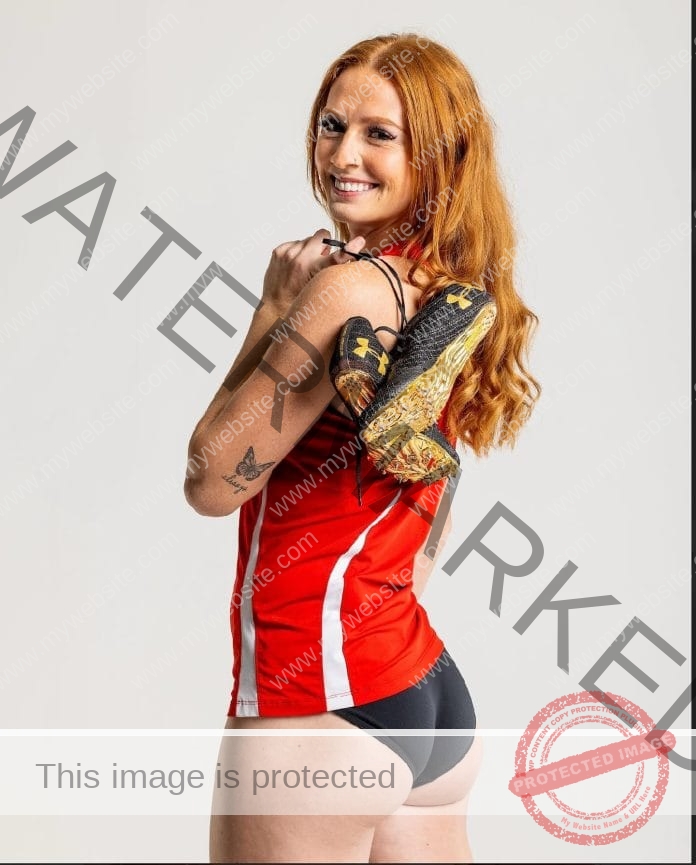 Kendall Holweg posing for a hpoto shoot in her red college track uniform, shows slung over her shoulder.