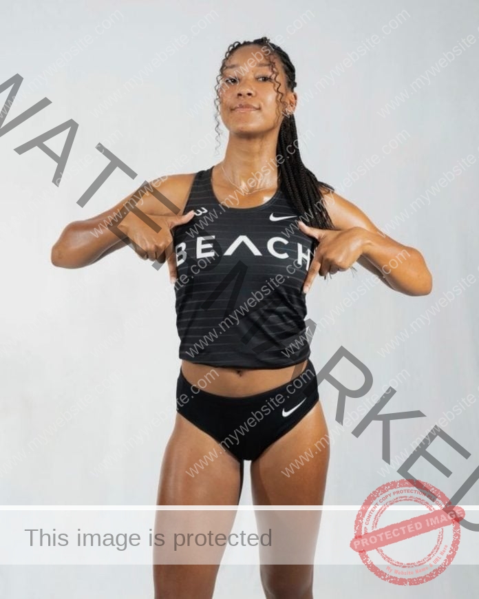 KiiKii Brown posing for a phot shoot in her college track uniform, in front of a white background.