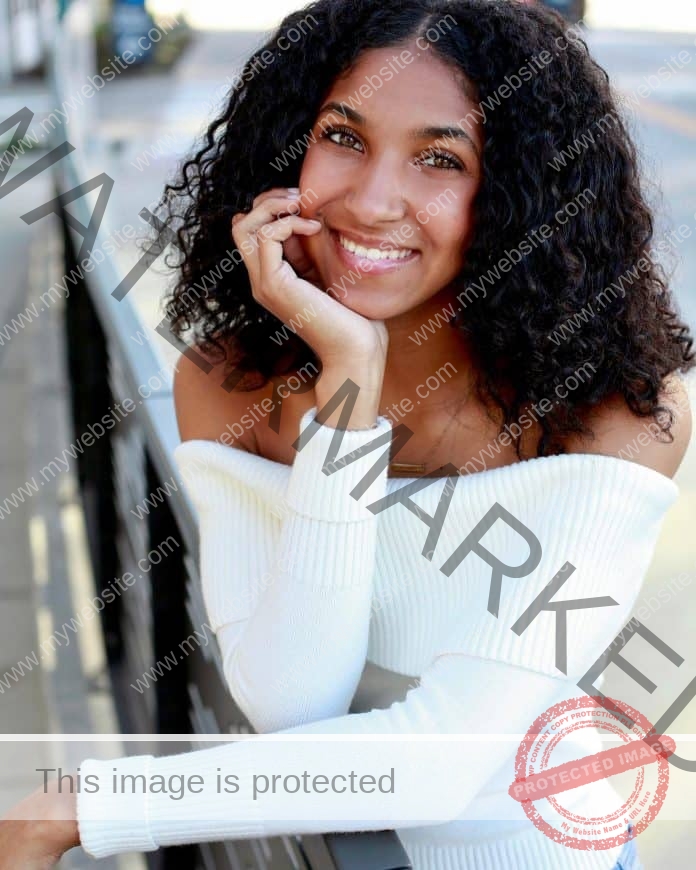 Kya Crooke posing for a photo in a white top and a big smile, head on her hand.