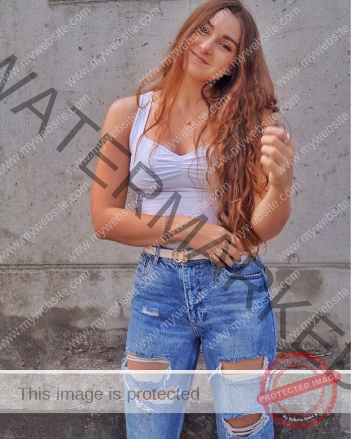 Lena Lackner posing for a photo in a white top and torn blue jeans.