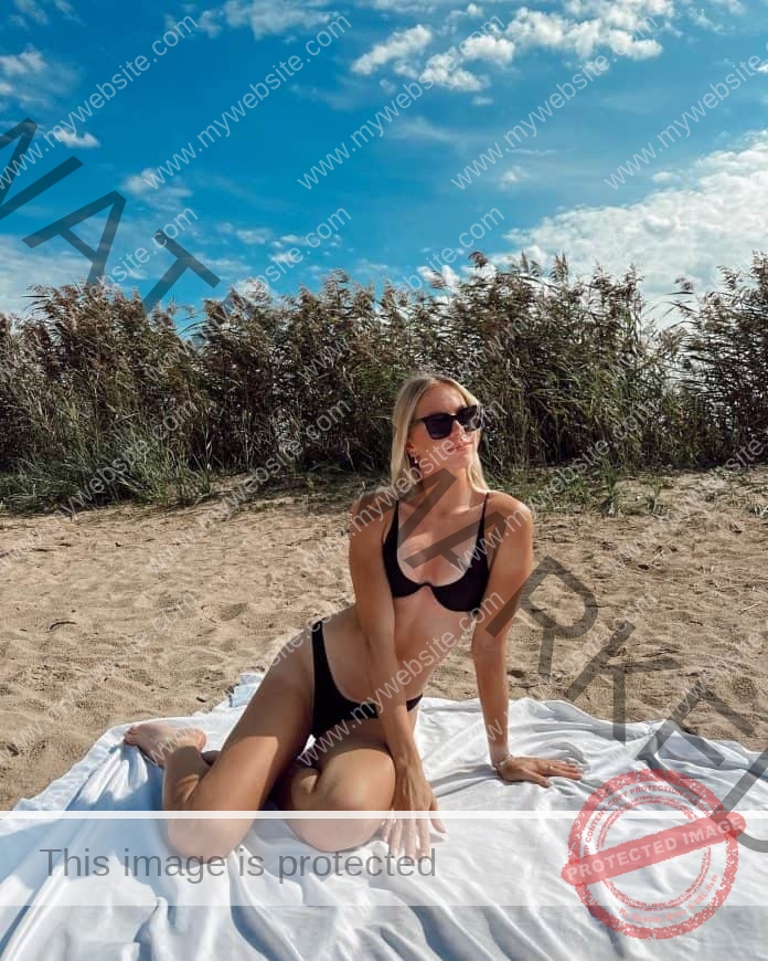 Liiljan Neerot of Estonia sitting on a blanket at the beach, wearing sunglasses and a black bikini.