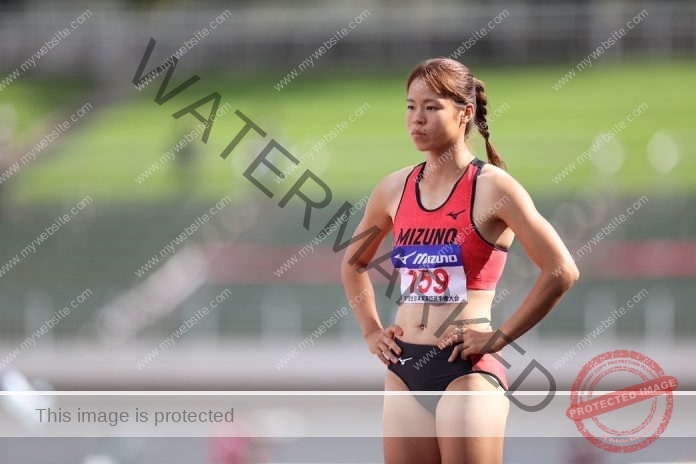 Maya Takeuchi stands ready for a race in her track uniform, wearing her name and number plate.