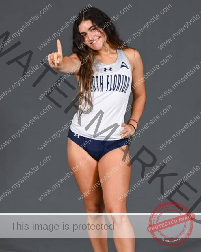 Rafaela Marchini stands for a phot shoot in her college track uniform, holding up a #1 finger.