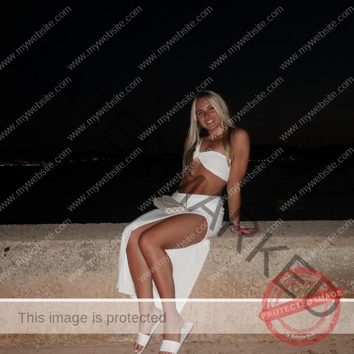 Jenna Hilditch sitting on a concrete divider in all white, with a long slit shite skirt and a white swimsuit top.