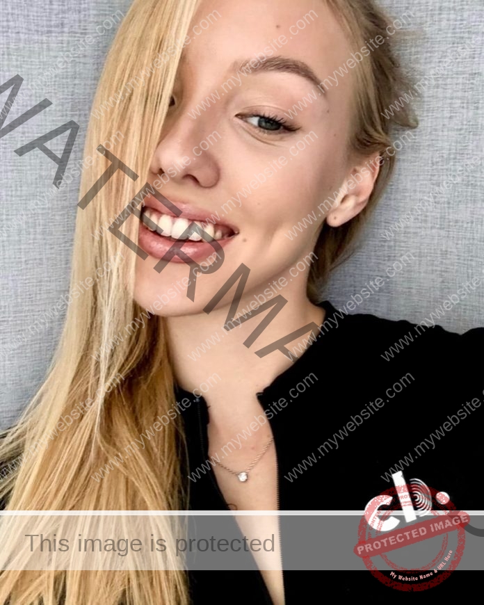 Sofia Yakushina posing for a headshot in front of a gray background, smiling big and wearing a black half-zip jacket.