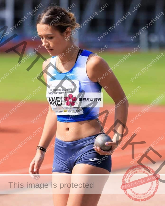 Victoria Anestik on the track wearing her competition uniform, holding a shotput and ready to compete.