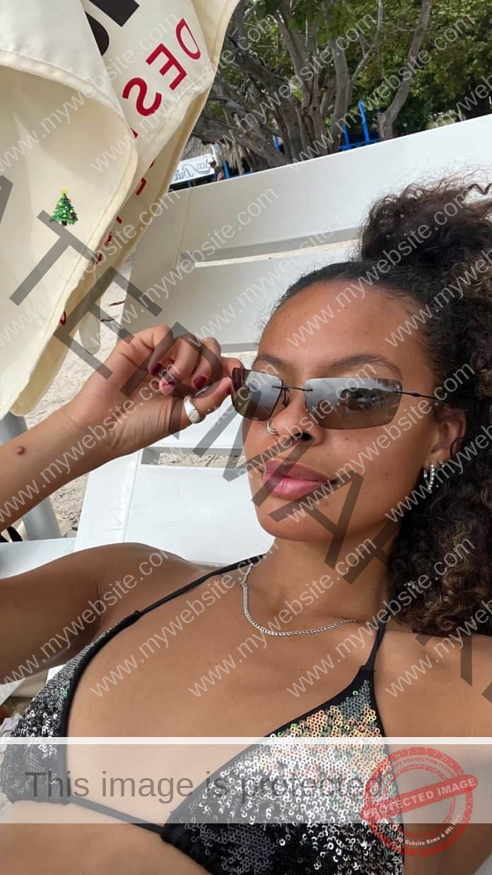 Havana Allistone-Greaves lounging in a pool chair, black and patterneed bikini top and looking over the top of her sunglasses.