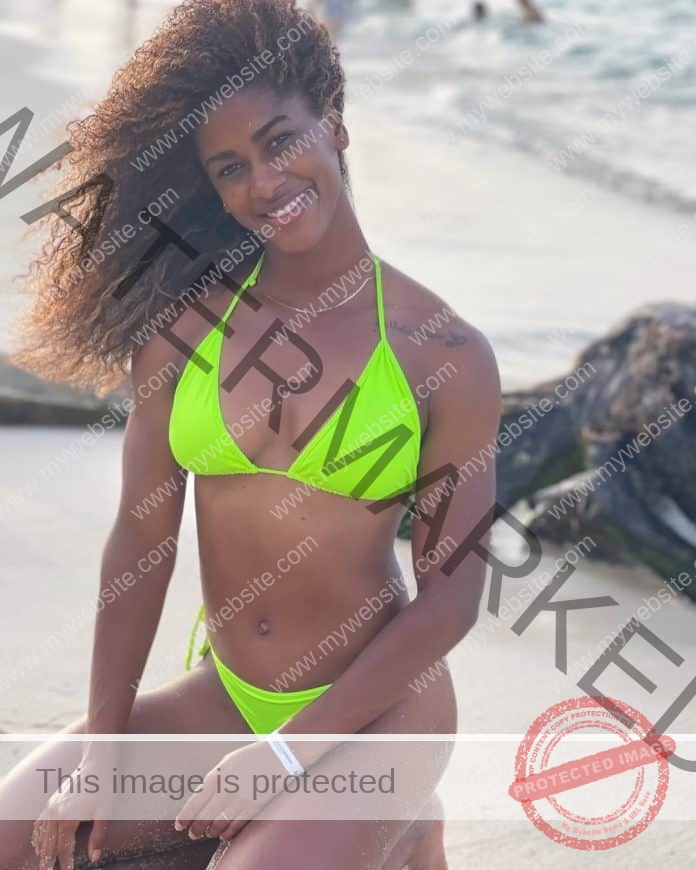 Anahi Suarez sitting on her knees at the beach, with a big smile, wearing a neon green bikini.