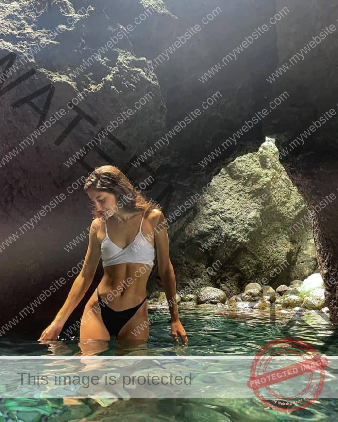 Ana Carrasco standing in a lagoon in a bikini, the sun glistening on her white bikini top and black bottoms.