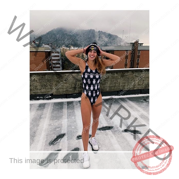 Jasynta Lampret, a track and field athlete from Australia, smiles in a patterned swimsuit, winter hat, and sneakers on a snowy rooftop.