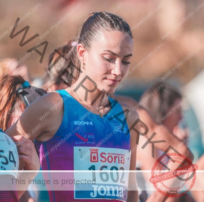 Anita Castro, a Spanish female track athlete, in blue and purple kit with bib 1602, stands focused among runners in Soria before a race.