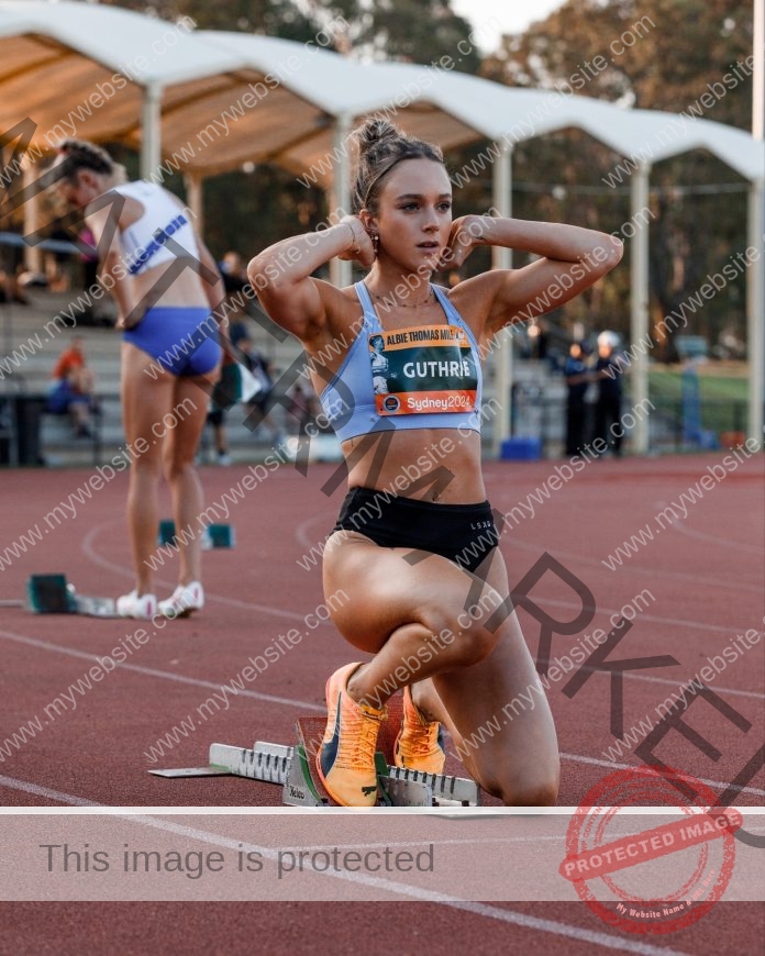 Leticia Arispe kneels at the starting blocks, focused and ready as another runner prepares in the background and spectators watch.