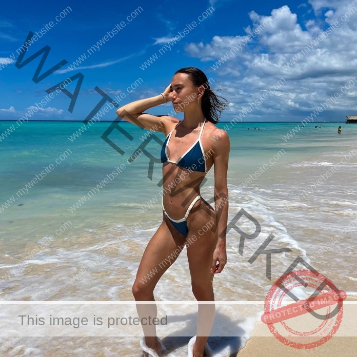 Catalina Rio Saraya, Argentina track and field athlete, poses on a beach in a blue bikini. Turquoise ocean glistens behind her.