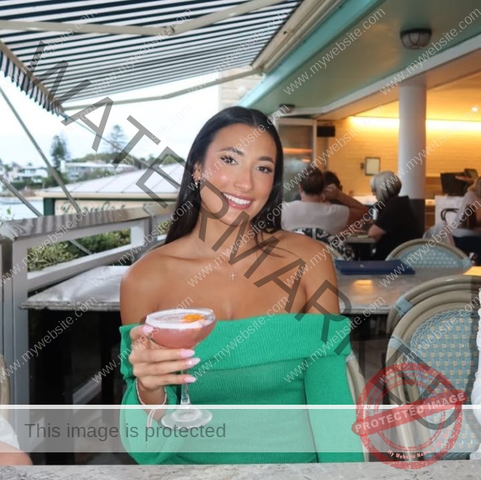 Woman in emerald dress enjoying cocktail at upscale rooftop restaurant with modern architecture.