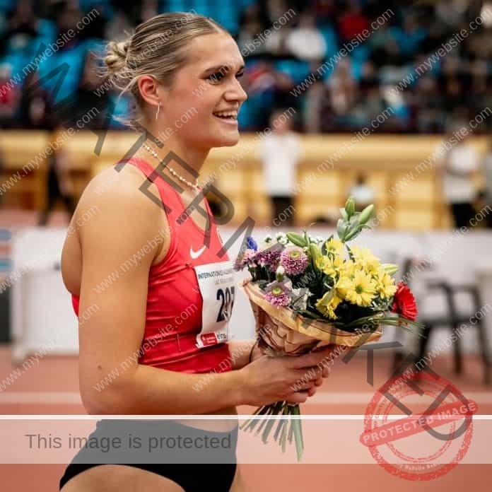 Franzi Schuster holding flowers after winning a race at the track, wearing a red track suit with name plate.