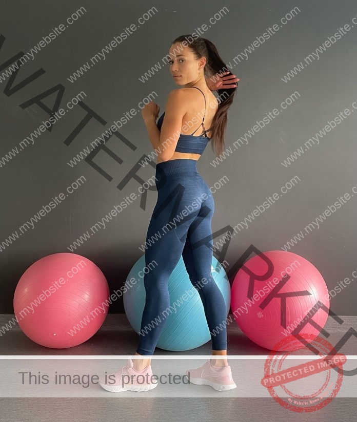 Katarzyna Martyna-Jurczyk in blue workout clothes and pink sneakers stands by three exercise balls, holding her long hair in one hand.