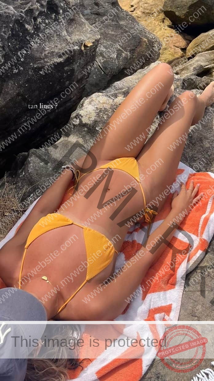 Liv Bloem lies oceanside, wearing a yellow bikini and hat.